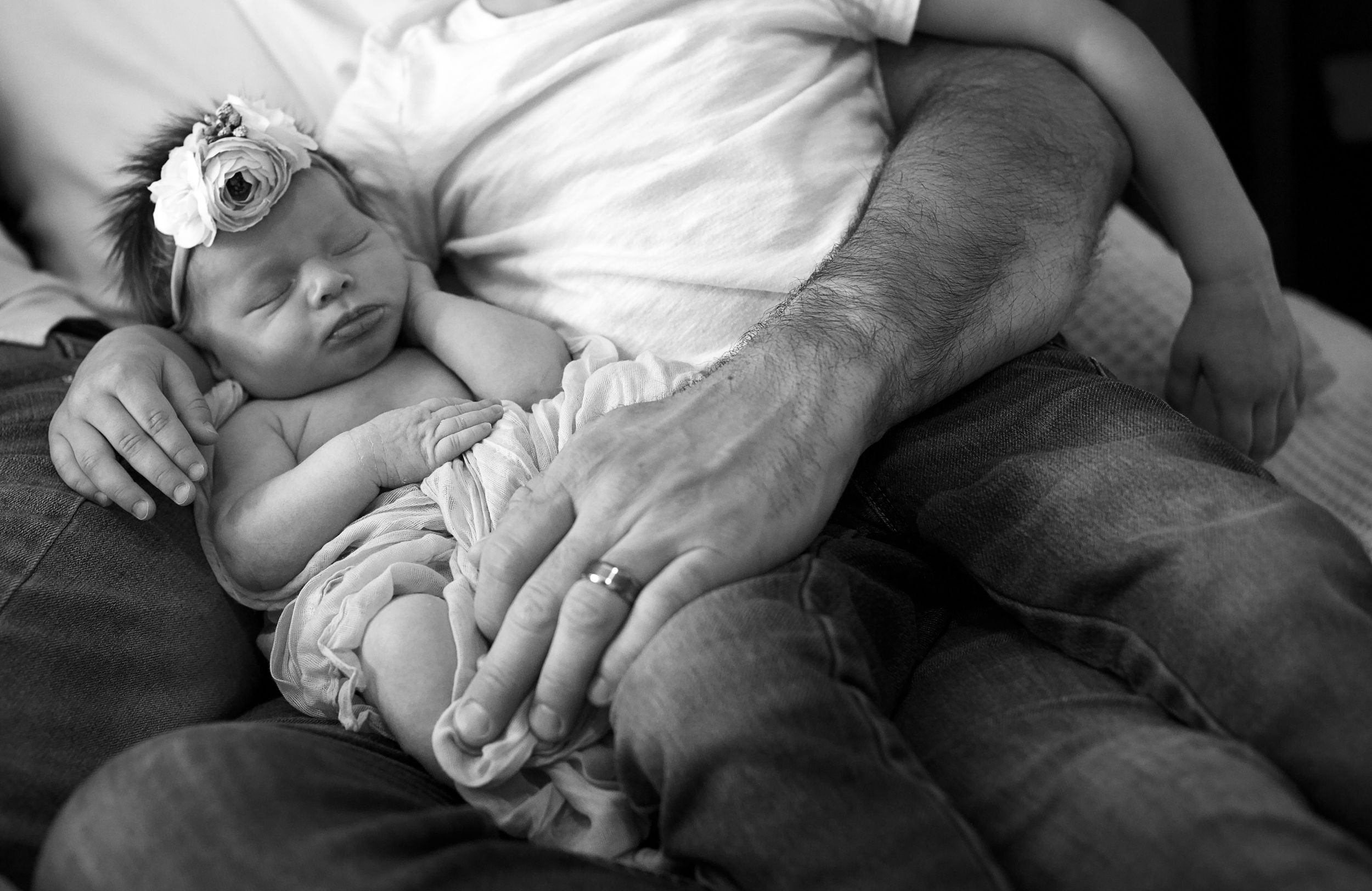Black and white photo of a sleeping newborn baby cradled in a grandfather's hands on his lap.