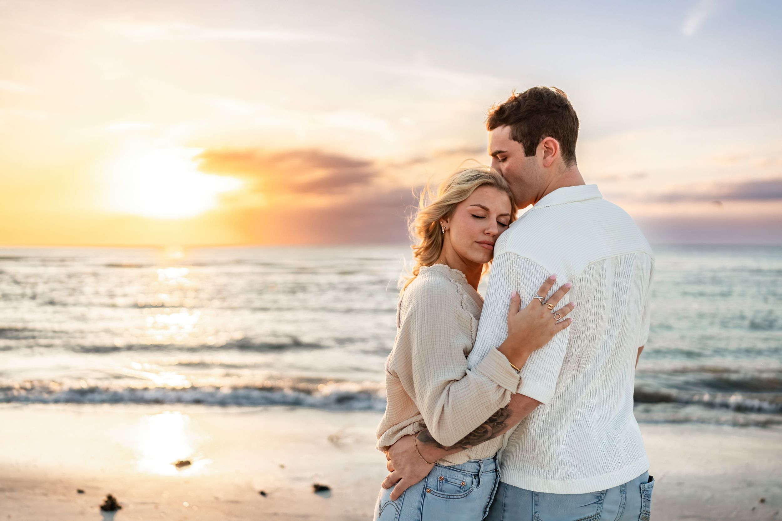 Romantic couple embracing on beach at sunset with ocean waves in background.