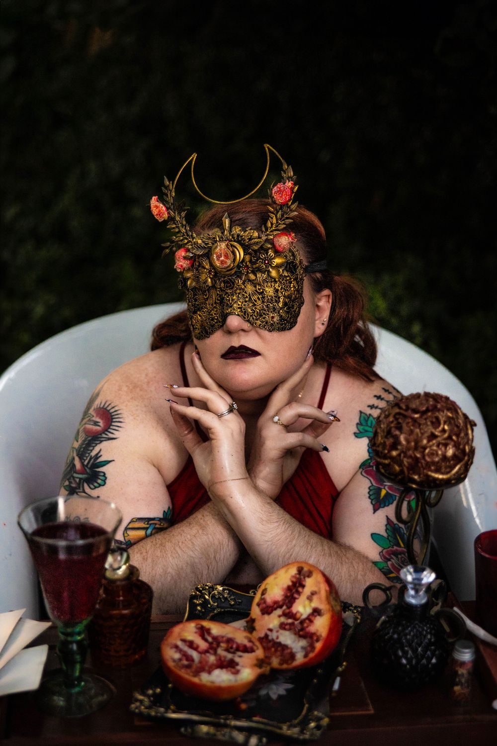 A woman dressed as Persephone poses in a red bath.