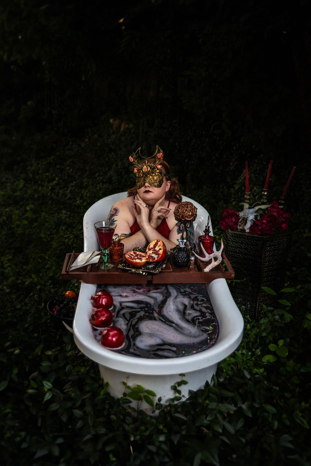A woman dressed as Persephone poses in a red bath.