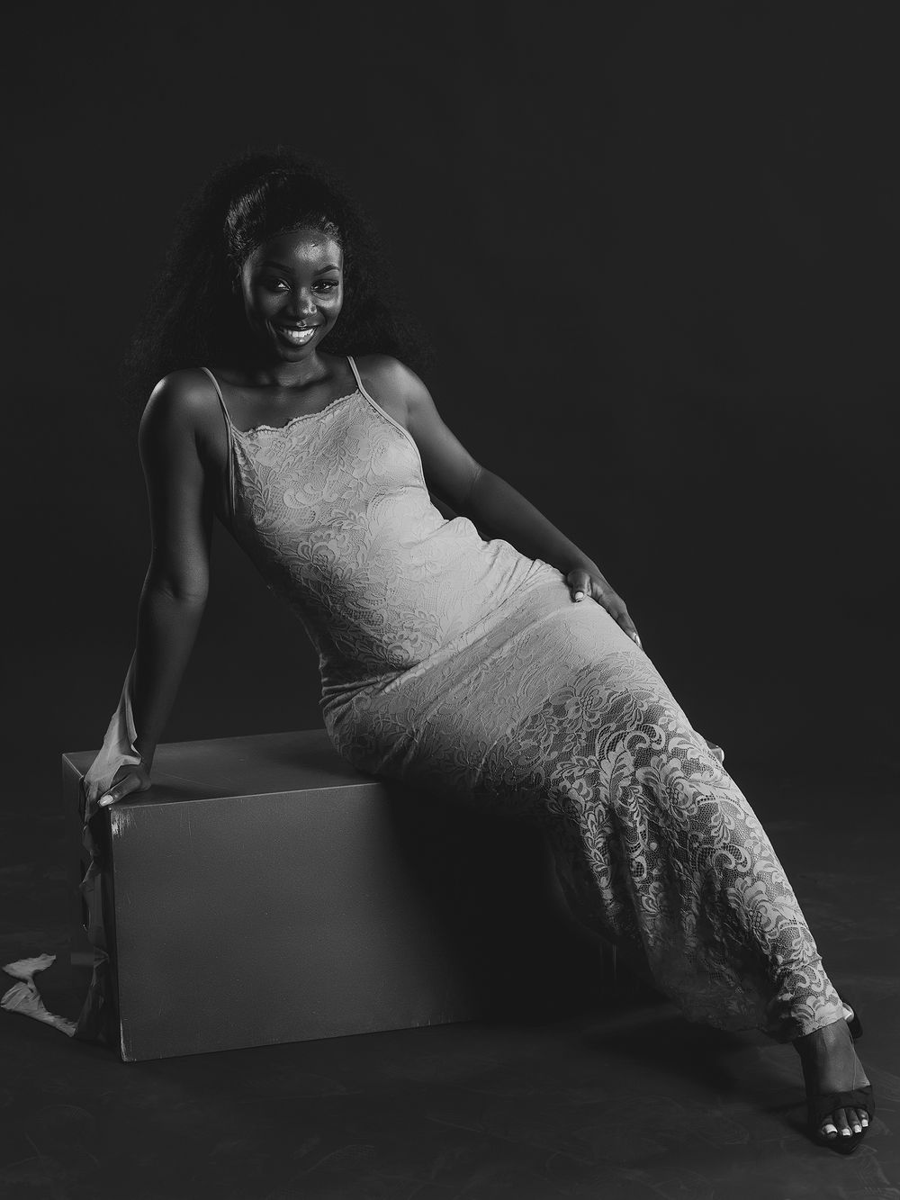 A dramatic black and white photo series showing someone in a white lace dress reclining on a dark background.