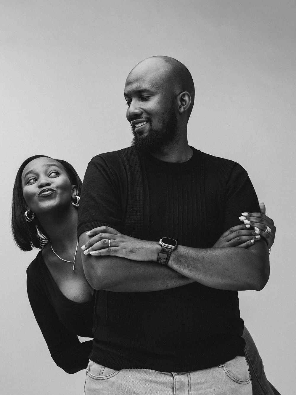 Black and white portrait of a playful couple sharing a joyful moment against a plain background.