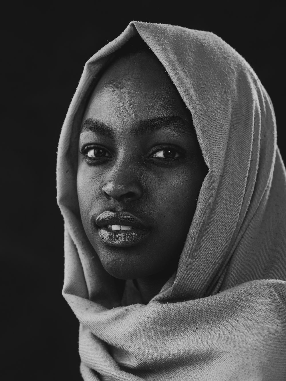 A dramatic black and white portrait series showing someone wearing a light cloth wrap against a dark background.