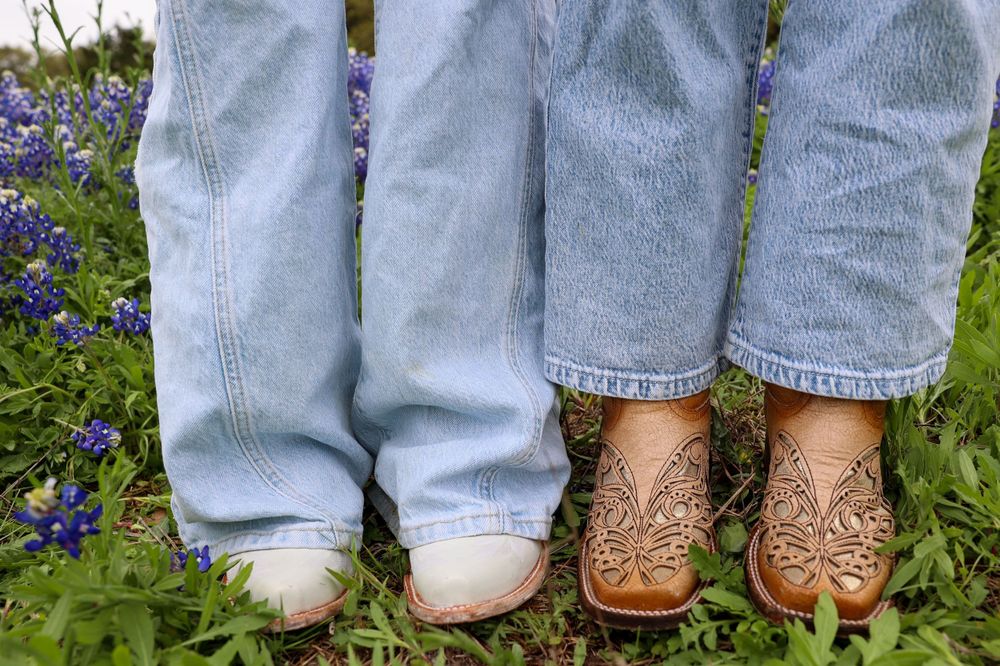 Two pairs of feet wearing jeans and boots sitting among bluebonnets.