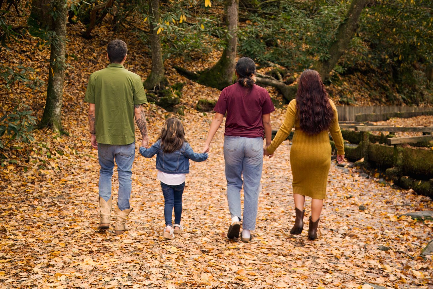 People walking together on a leaf-covered forest path during autumn season with fallen orange leaves.