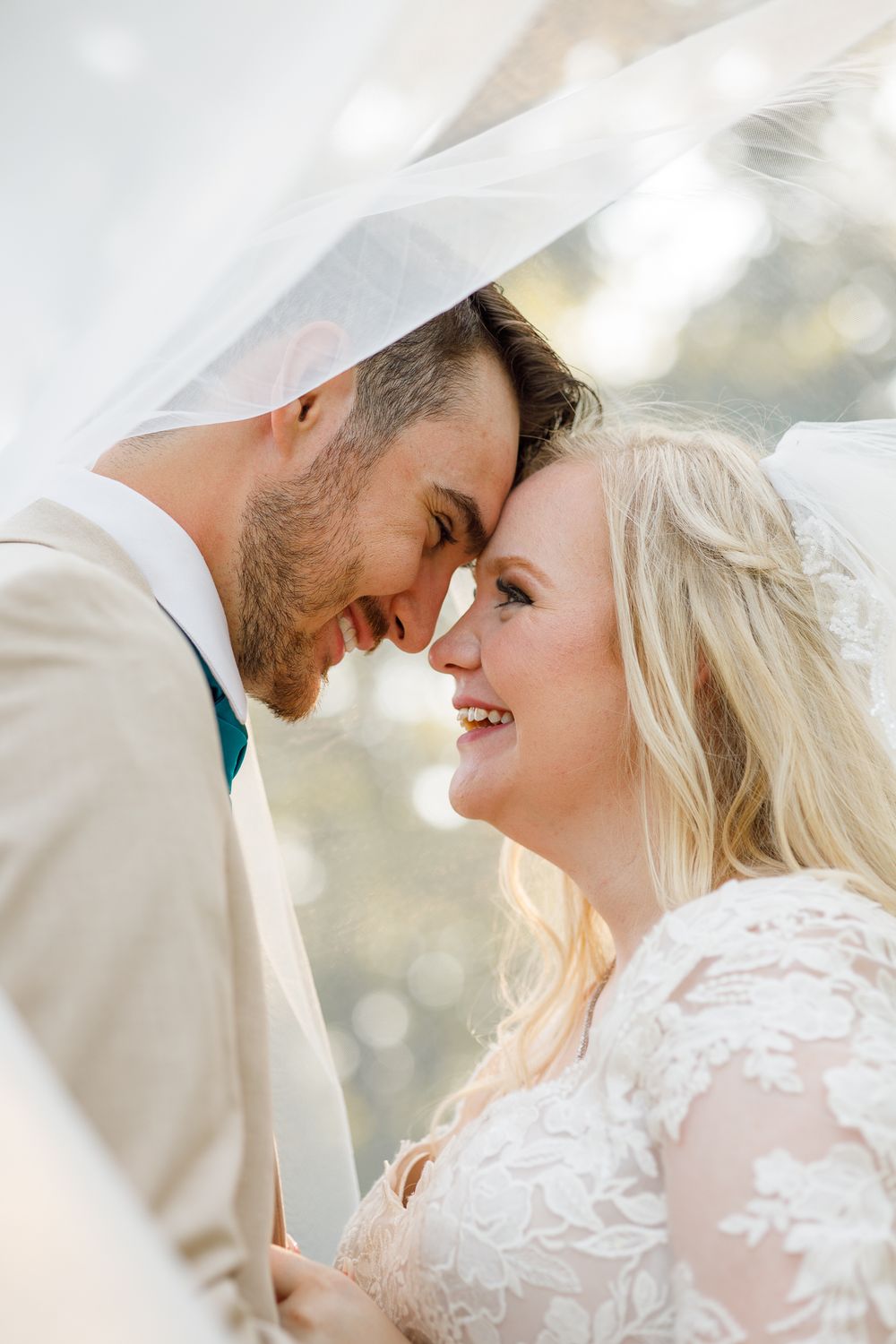 Romantic wedding portrait of a couple in white attire sharing an intimate moment under a veil.