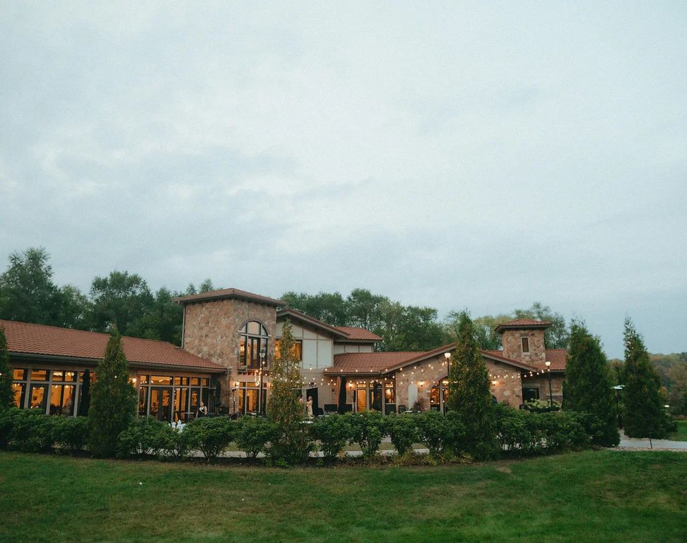 Rustic stone and wood luxury estate building with landscaping set against trees and cloudy sky.