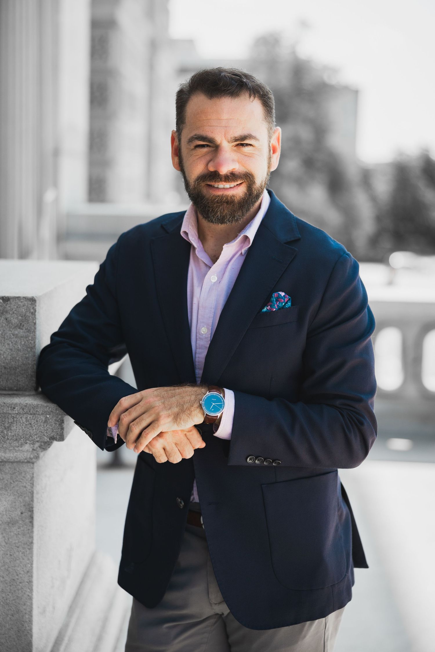 Professional in navy blazer and pink shirt smiling against architectural backdrop.