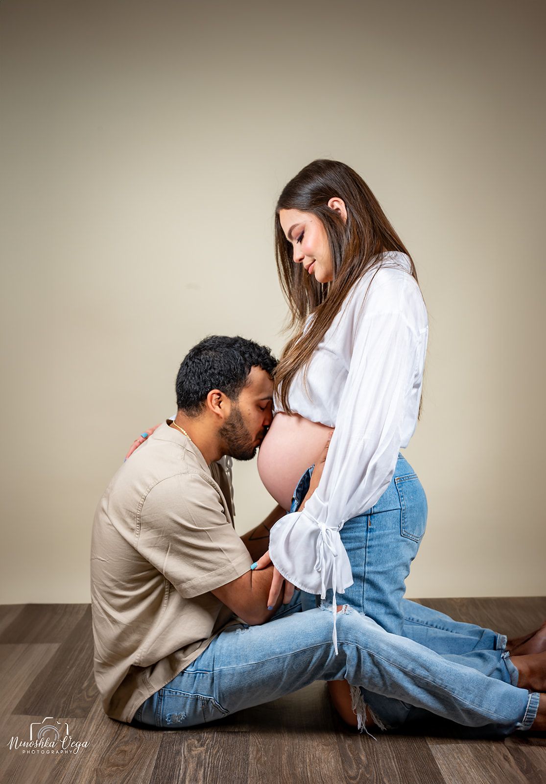 Intimate maternity photography session with couple on wooden floor.