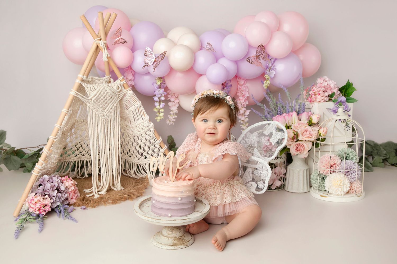 Cake smash setup with macrame teepee, pink balloons, and boho decorations.