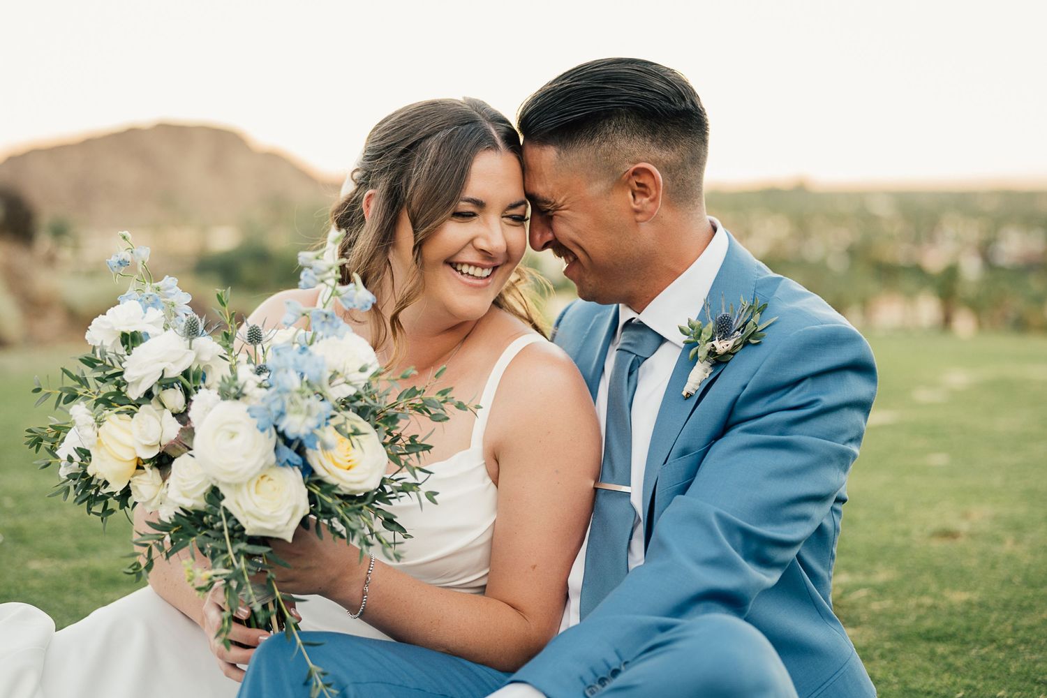 Wedding couple sharing intimate moment with white floral bouquet against mountain landscape.