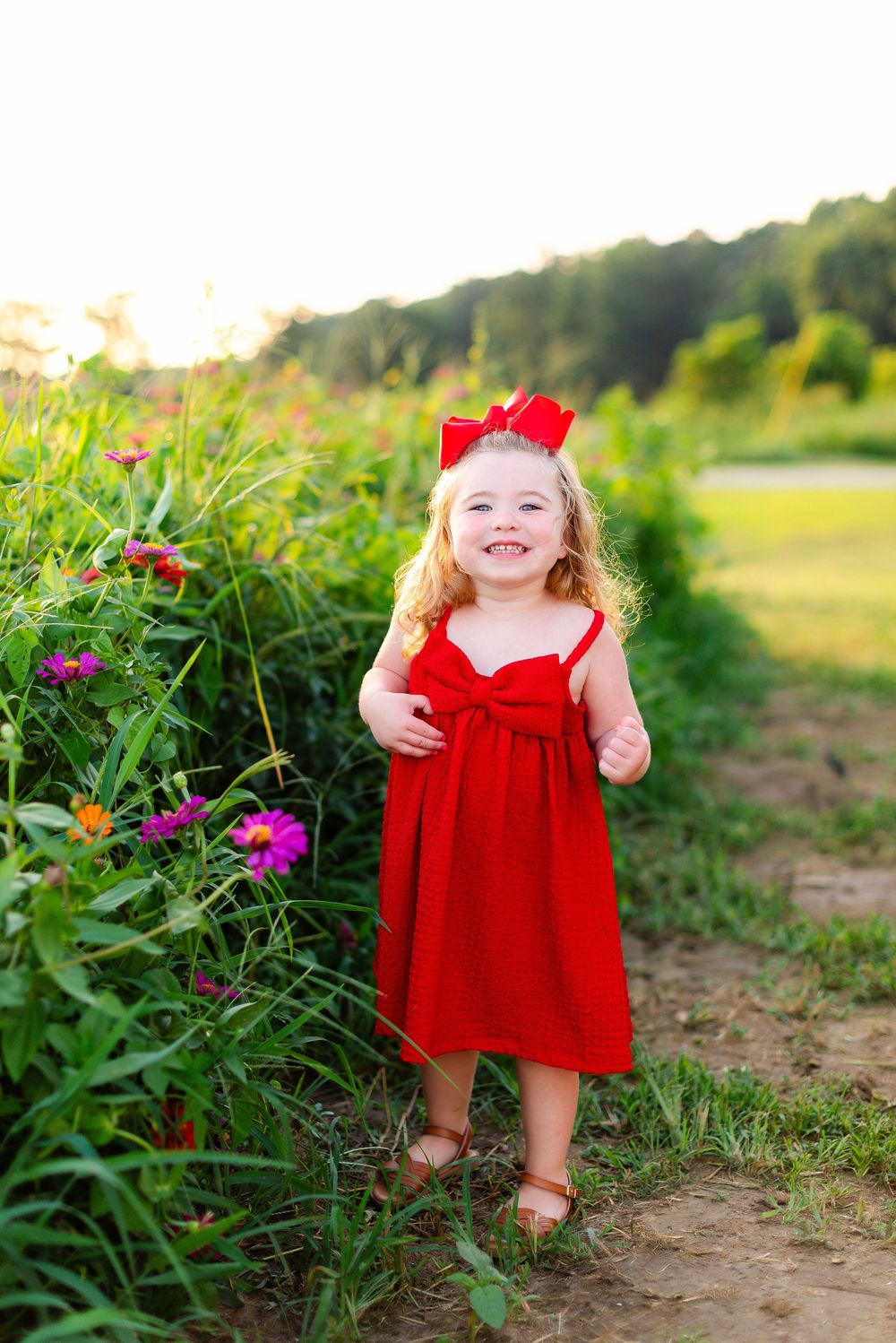 A bright red dress stands out against a garden path bordered by vibrant wildflowers and greenery on a summer day.