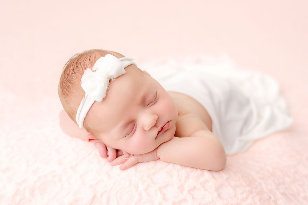 Newborn baby sleeping peacefully on soft pink blanket while swaddled in white wrap.