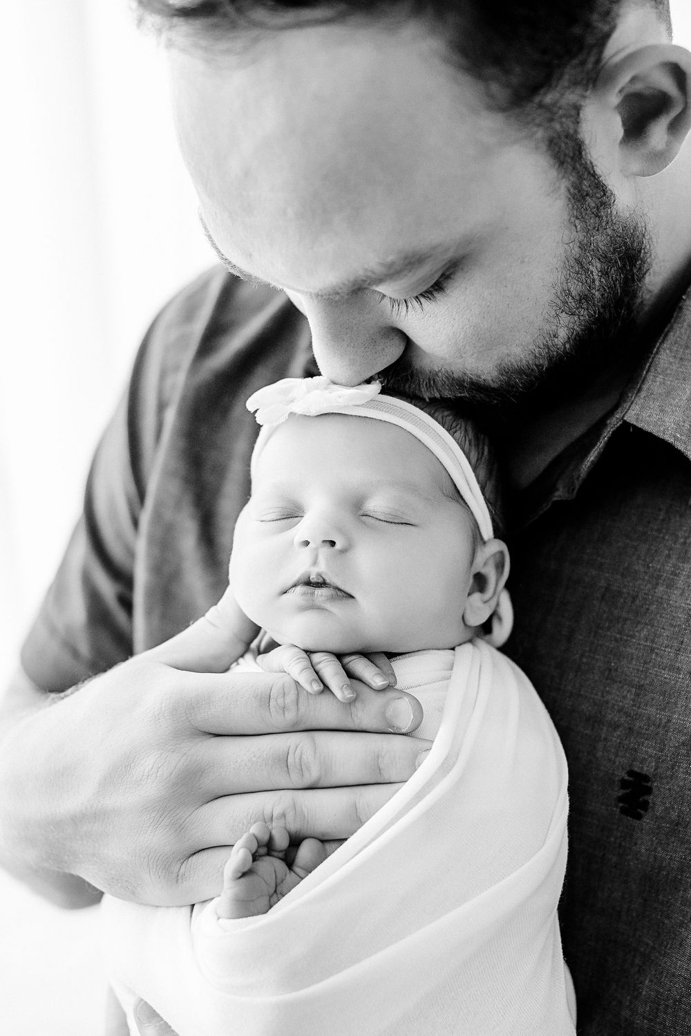 A black and white photo series showing a close-up tender moment between a bearded parent and sleeping baby.