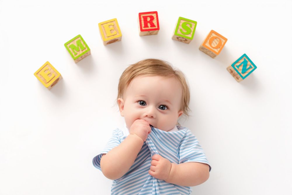 A baby in blue stripes lies on a white surface near colorful alphabet blocks arranged in a curved line.