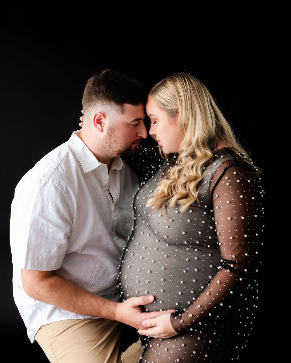 Maternity couple poses in black and white with white polka dot sheer overlay on dark background during intimate photo shoot.