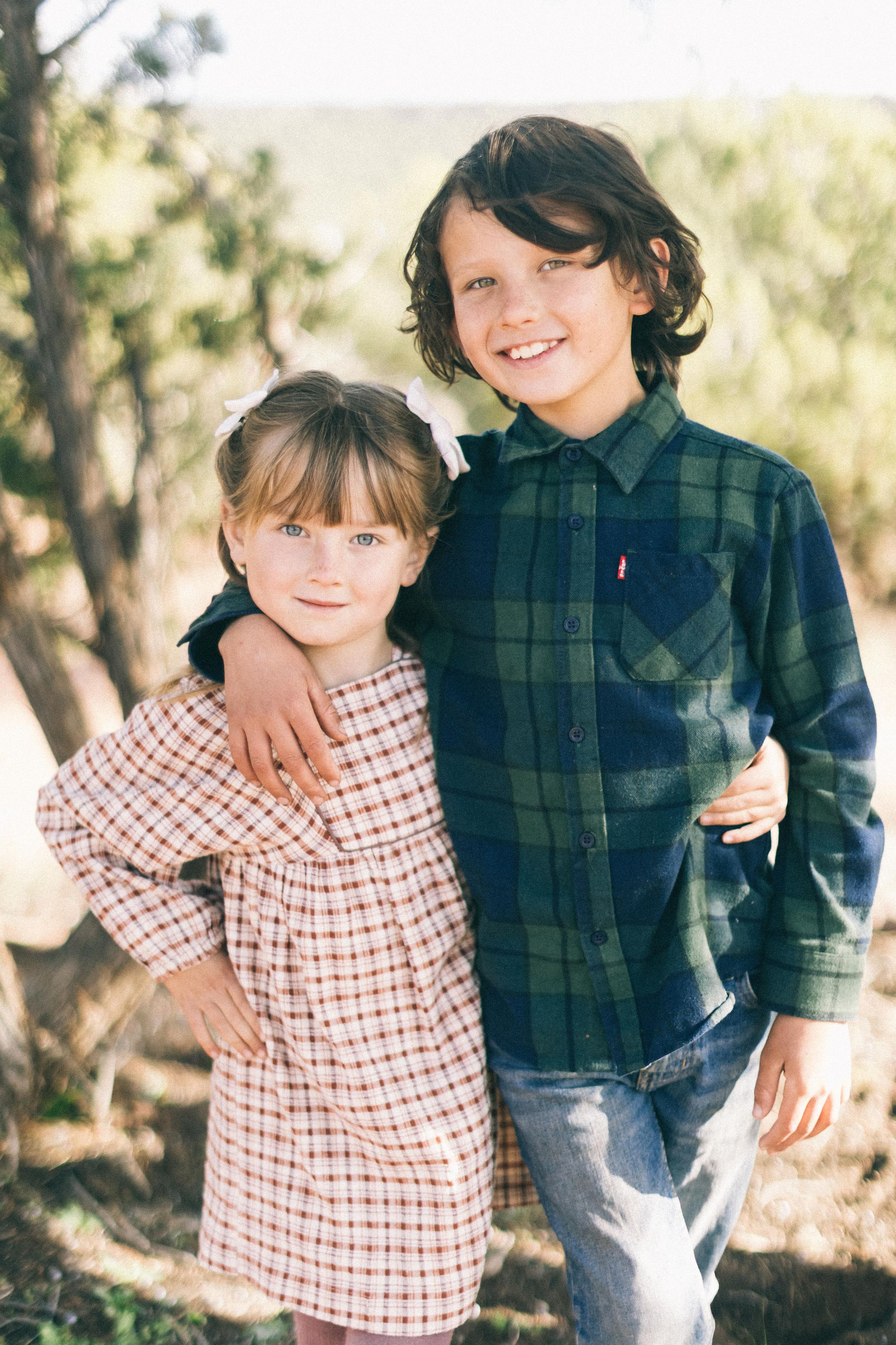 Two young people pose together outdoors wearing plaid and gingham patterns.