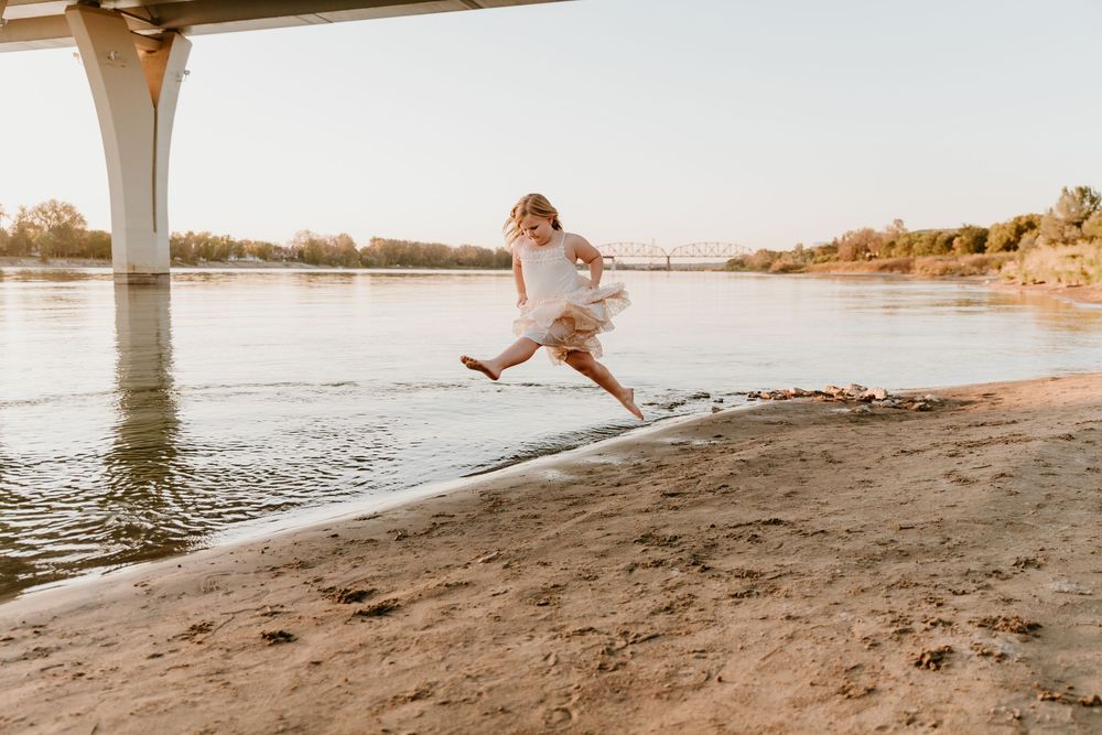 Multiple shots of someone in a light dress jumping and playing along a sandy beach at golden hour.
