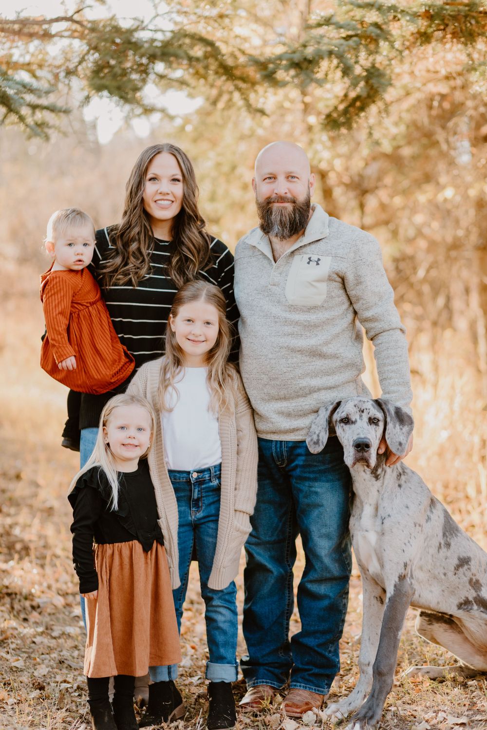Family portrait in autumn setting with dog and warm casual attire.