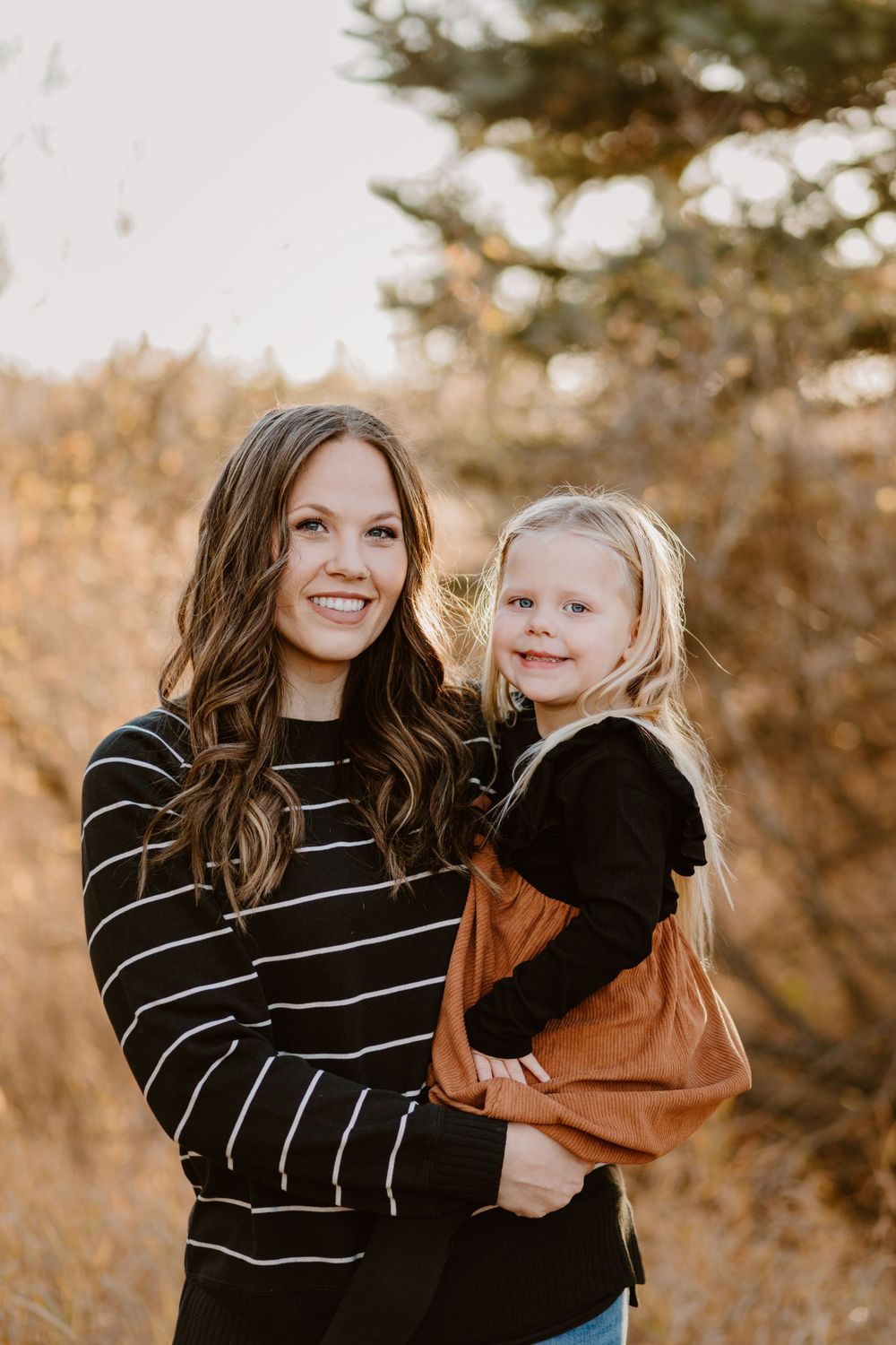 Parent and child in matching warm autumn tones pose together in forest setting.