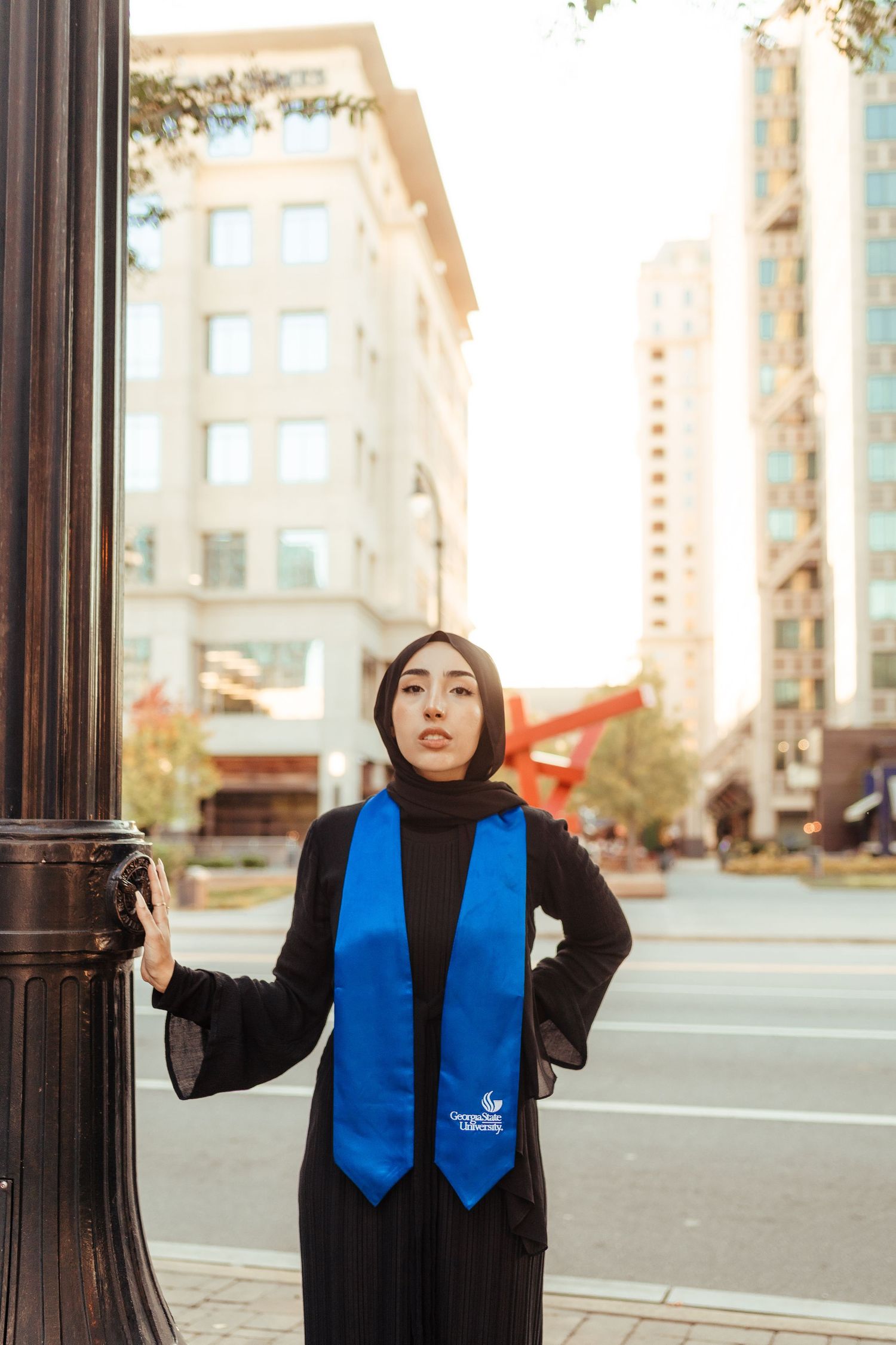 A graduation photo featuring a blue stole against an urban backdrop.