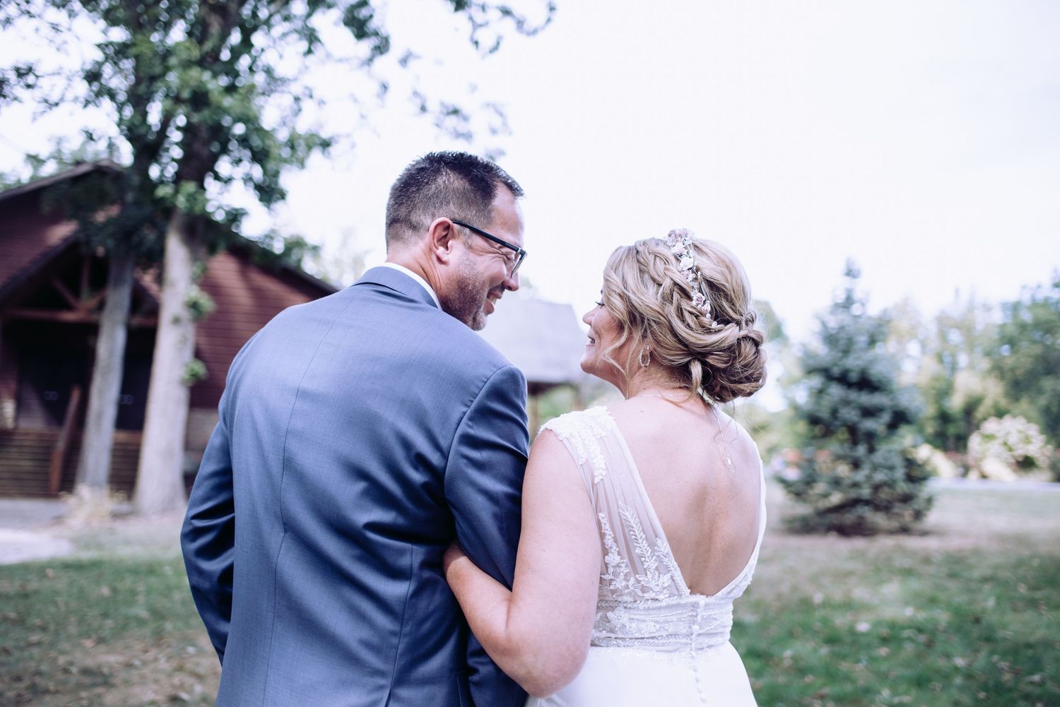 A couple in wedding attire share an intimate moment while walking outdoors in a natural setting.