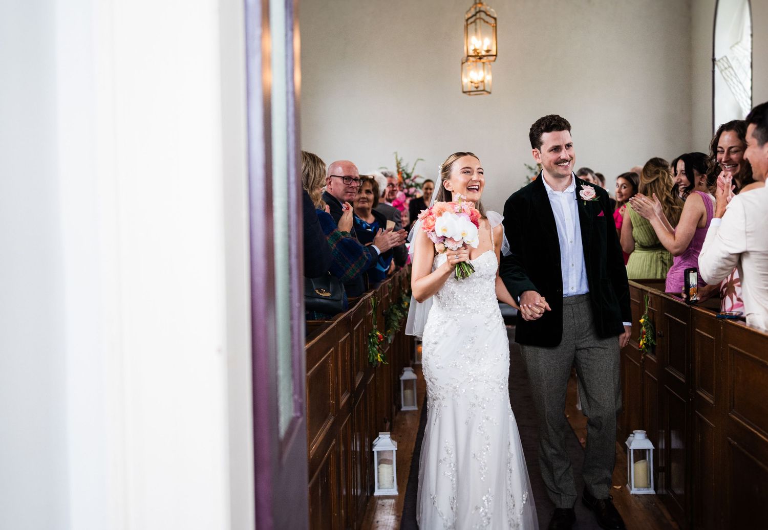 Black and white photo of newlyweds walking through crowd of celebrating wedding guests.