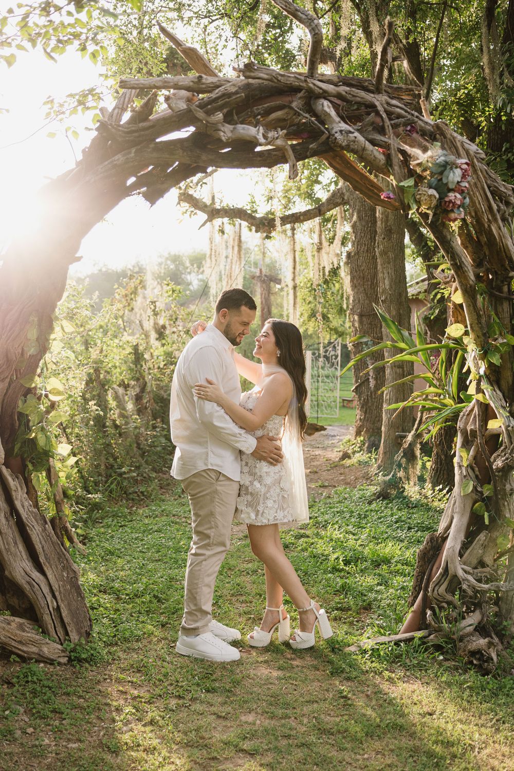 Romantic couple poses together in a lush garden setting with sunlight filtering through trees.