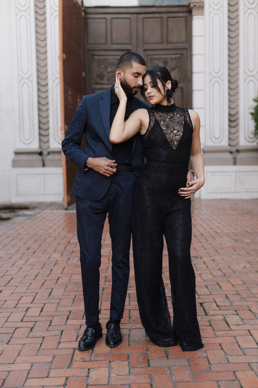A romantic couple embraces in formal wear against a classic brick and column backdrop.
