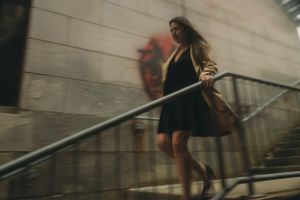 A woman in a dark dress and jacket walks up concrete stairs in motion blur.