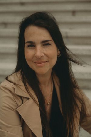 A portrait of a woman in a beige coat smiling warmly at the camera.