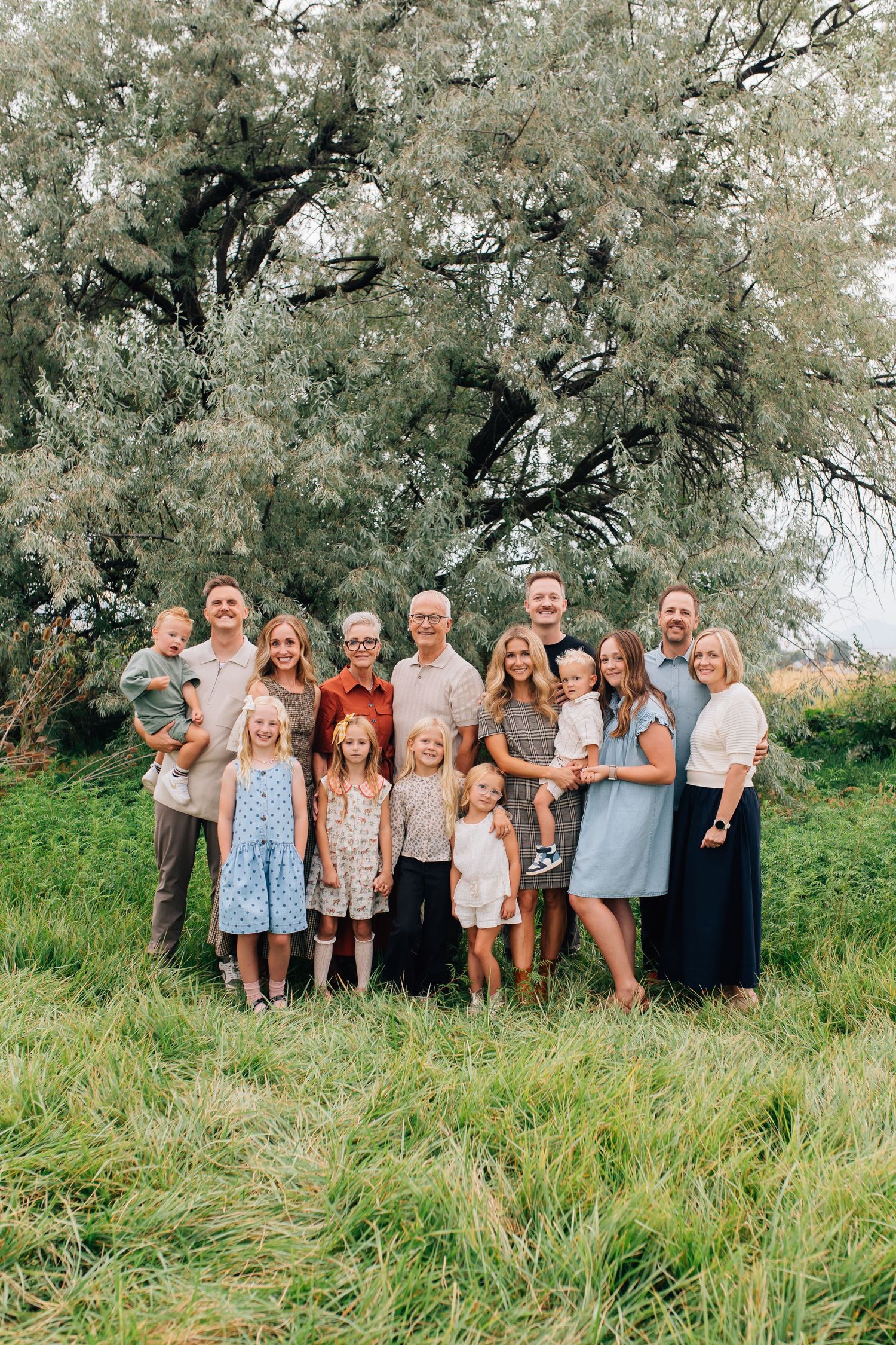 Extended family poses together for group portrait in front of autumn foliage.
