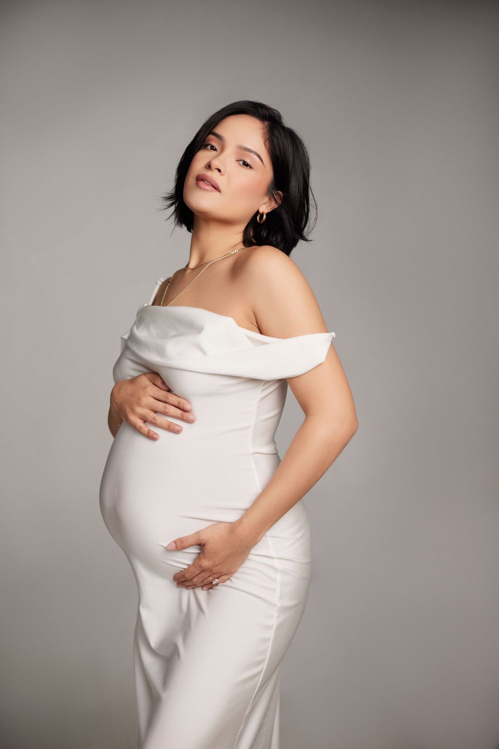 Minimalist maternity photoshoot with white fabric wrapping against grey background.