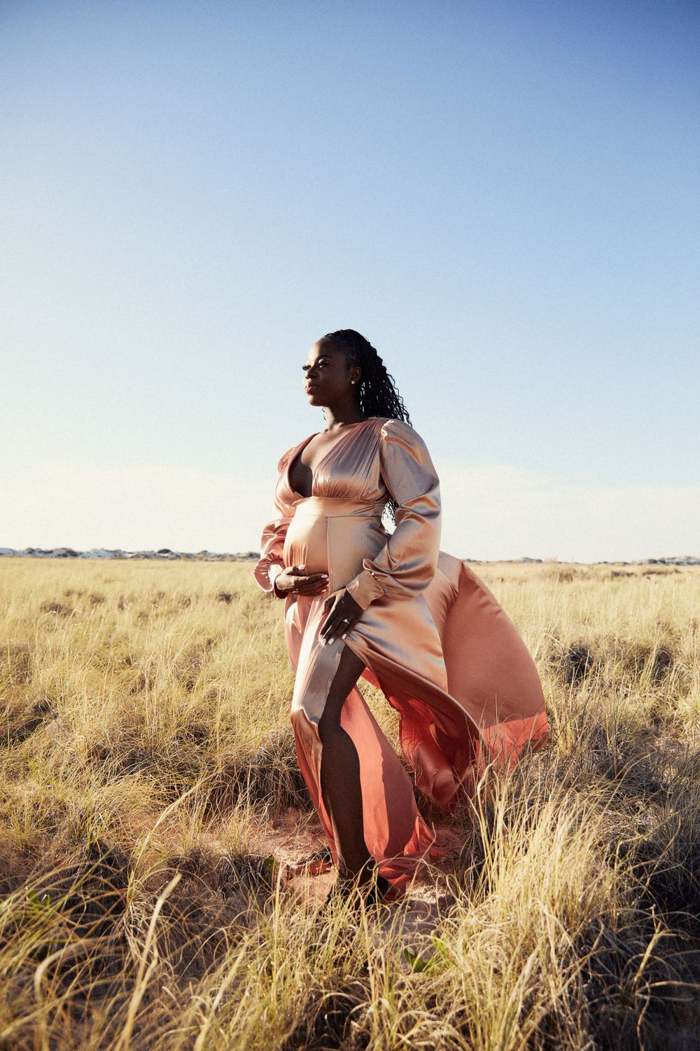 Dramatic outdoor photoshoot in tall grass field with flowing coral dress at golden hour.