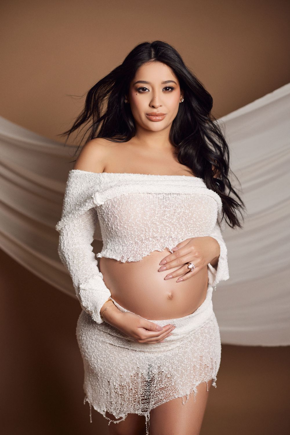 Elegant maternity portraits featuring off-shoulder white lace against brown background.