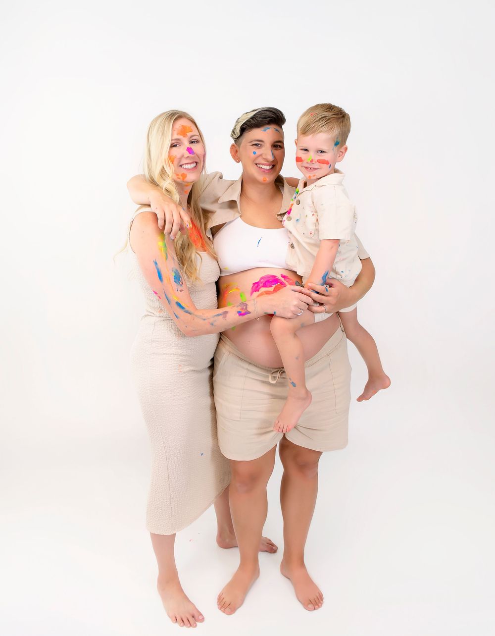 A family wearing matching beige outfits poses together in a bright studio setting for a playful portrait series.