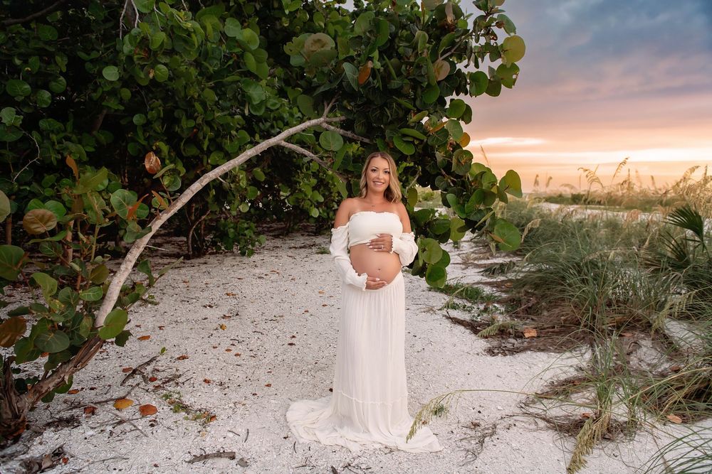 A serene beach photoshoot scene with white sand and tropical foliage at sunset.