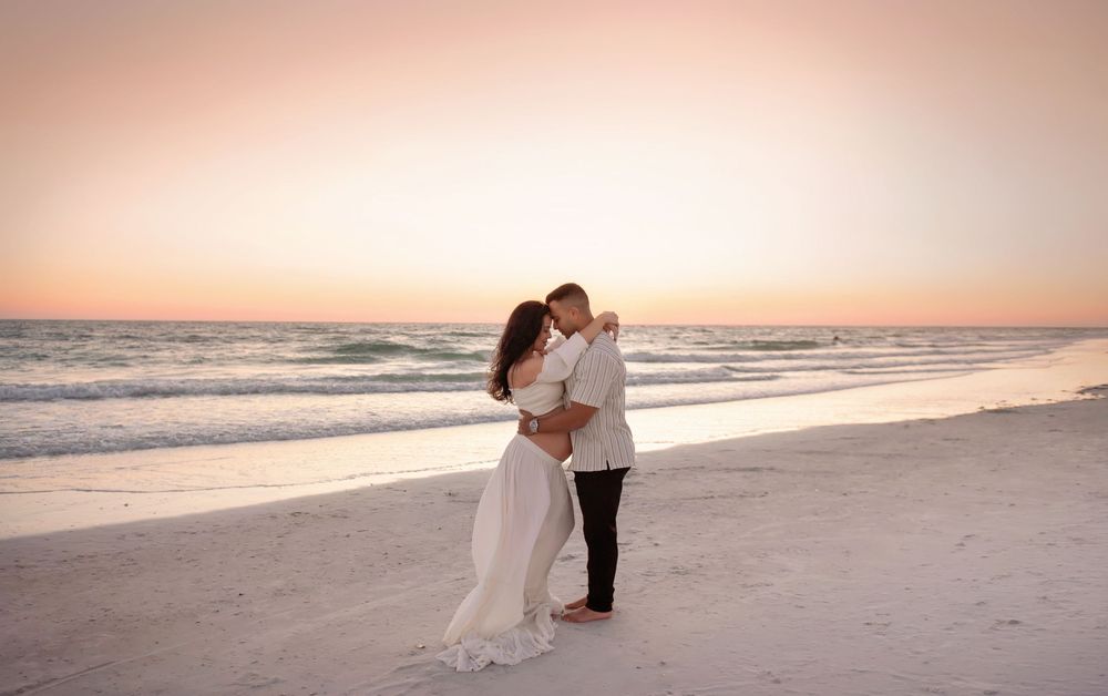 Couple sharing a romantic kiss on a white sand beach at sunset, bride in flowing white dress.