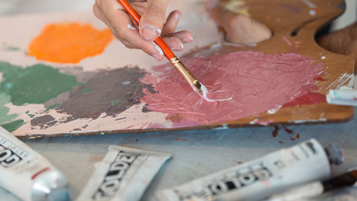 Close-up of an artist's hand mixing paint colors on a palette.