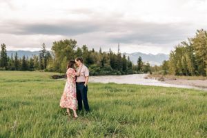 A couple shares a romantic moment in a green field beside a winding river.