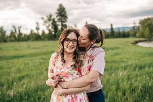 Two people embrace while sharing a tender moment in a mountain meadow.