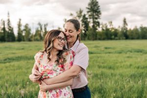 A couple shares an intimate embrace in a green field with mountains in the distance.