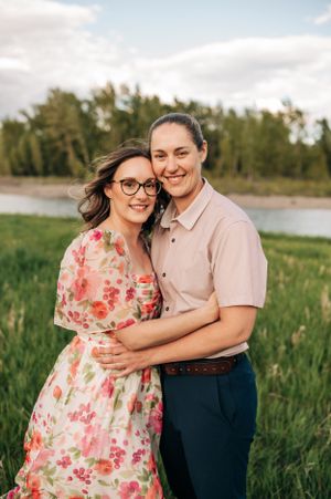 A couple shares a tender moment outdoors in a floral dress and casual attire by a scenic river.