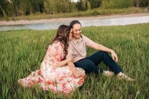 A couple relaxes in a grassy field sharing a candid moment of laughter together.