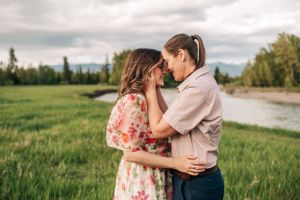 A tender moment between a couple in a scenic field with mountains and river in the background.