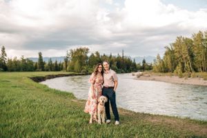 A couple poses with their golden retriever by a winding river during an outdoor photoshoot.