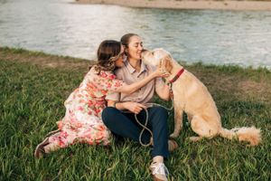 A couple shares a joyful moment with their golden retriever by the river.