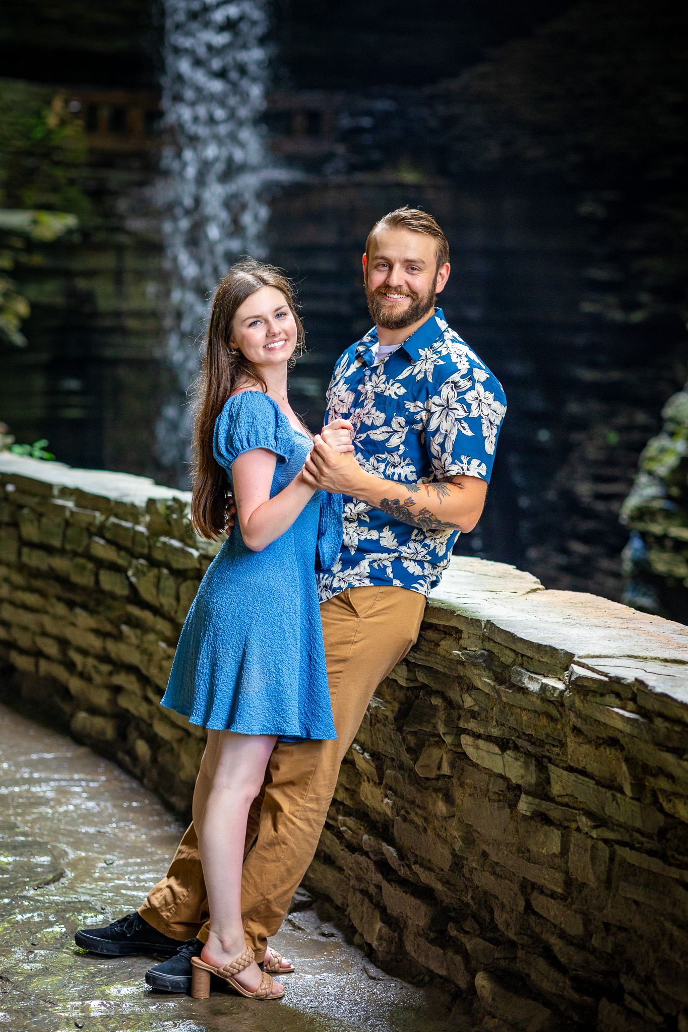 Couple in matching blue outfits embrace near scenic waterfall backdrop.