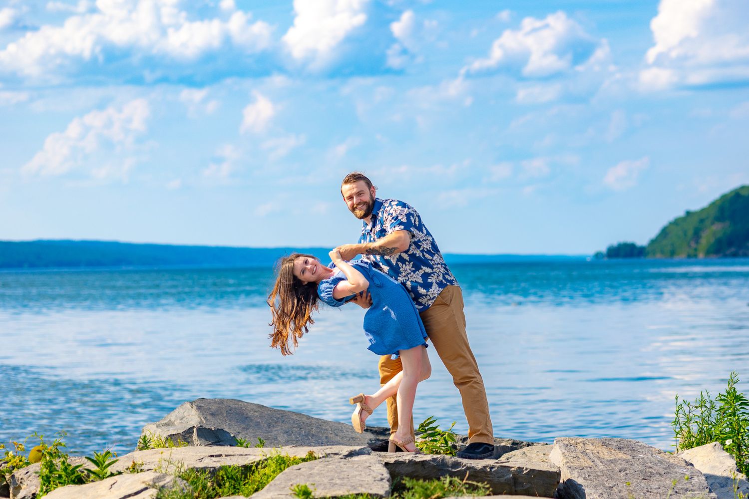 Playful couple in coordinating outfits pose dramatically on coastal rocks.