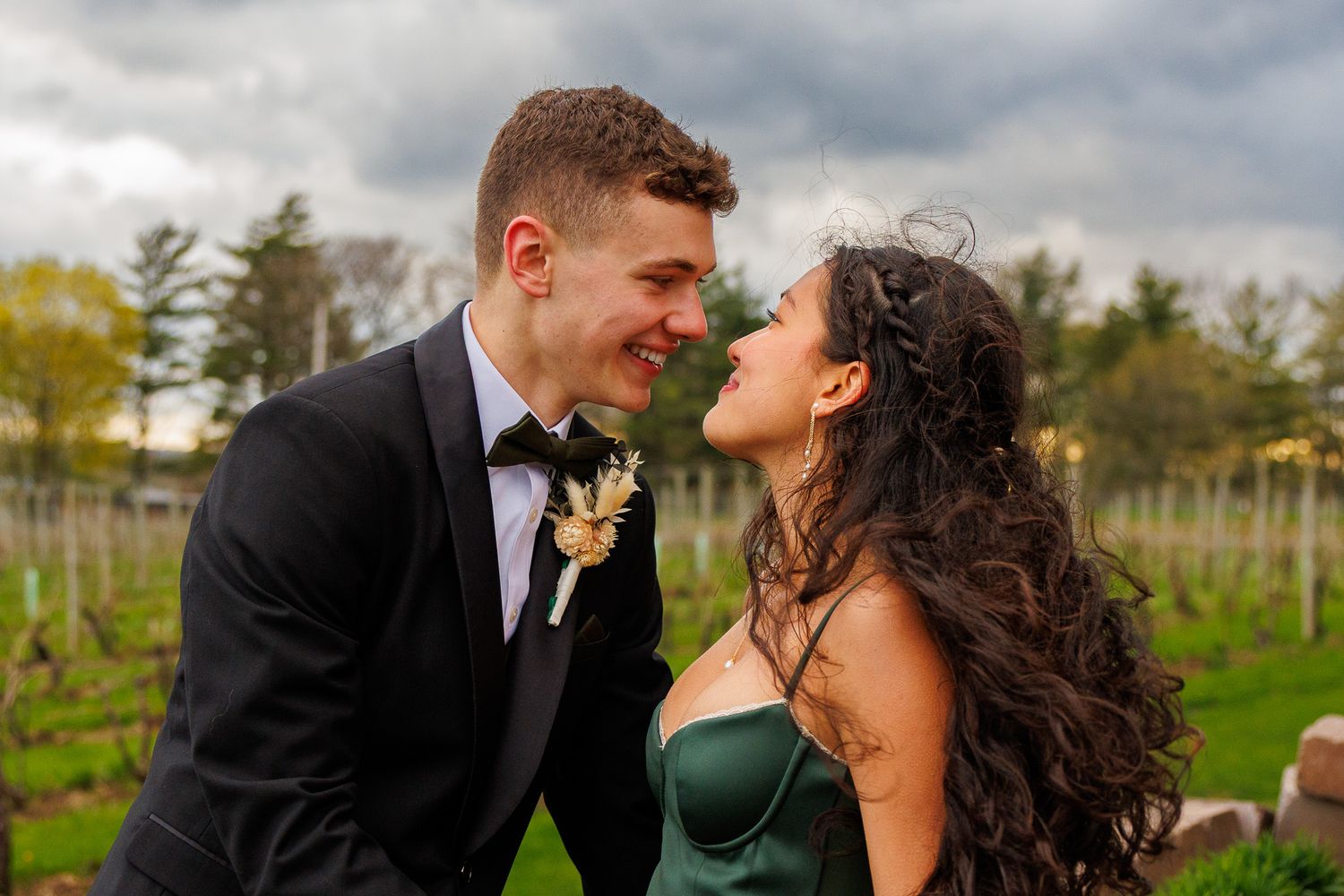 A happy couple shares an intimate moment in their formal attire against a scenic vineyard backdrop.